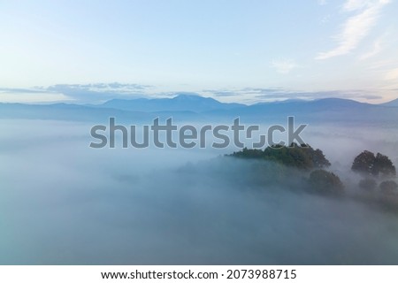 View from above, stunning aerial view of a forest surrounded by fog with a mountain range in the distance.
