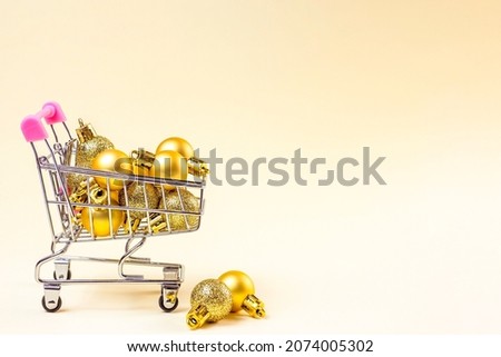 Trolley shopping cart with golden Xmas baubles on light background with copy space. Christmas sale, discounts, holiday shopping and buying gifts and presents concept.