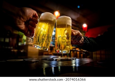 two glass of beer in hand. Beer glasses clinking in bar or pub Royalty-Free Stock Photo #2074016366