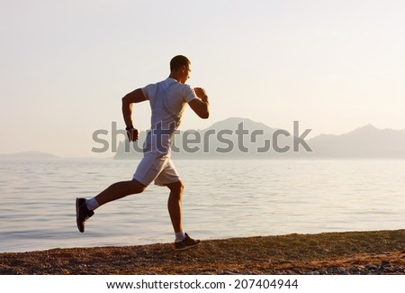 Jogger  in fitness clothing running along beach coast with the blue sky in the background and open space around him