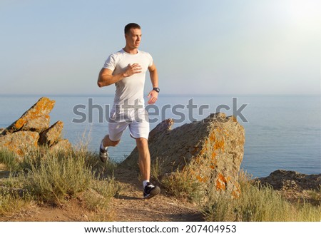 Young man in fitness clothing running along mountain beach