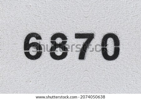 Black Number 6870 on the white wall. Spray paint. Number six thousand eight hundred and seventy.