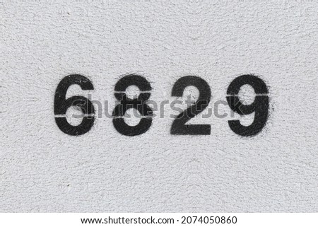 Black Number 6829 on the white wall. Spray paint. Number six thousand eight hundred and twenty nine.