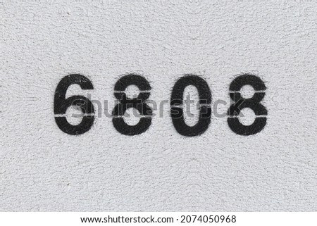 Black Number 6808 on the white wall. Spray paint. Number six thousand eight hundred and eight.
