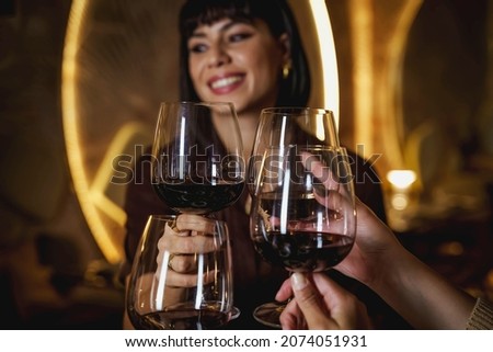Woman clinking wine glasses celebrating birthday at restaurant - group of friends toasting red wine at cafe - focus on the glasses on the front
