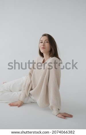 Cool sporty girl in beige sweater and white bicycle pants on neutral grey background. Soft light, monochrome picture. Good vibes, positive emotions. Tall and slim european model in good shape.