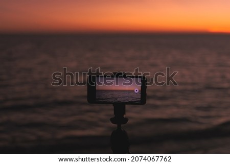 Smart phone put on tripod for take a video of sea at the sunset. Beautiful scenery