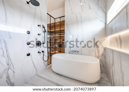 Bathroom and walk in closet with white marble oval tub blue sky windows fireplace sinks an lighting Royalty-Free Stock Photo #2074073897