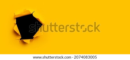 Bright yellow torn paper inside a black hole in a hole. Banner Royalty-Free Stock Photo #2074083005