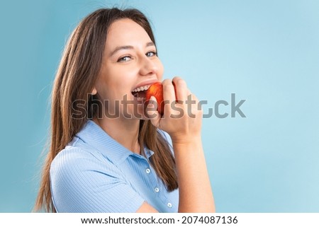 Young woman eating an apple over blue background. Healthy nutrition, diet food concept. Beautiful young woman eating an organic fresh red apple. 
 Royalty-Free Stock Photo #2074087136