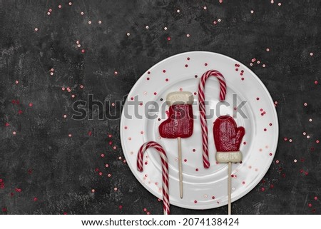 Merry Christmas and Happy Holidays greeting card, banner. Lollipops on a plate. New year table setting. Horizontal dark background top view. Concept of greetings, table setting, decor. Sparkles. 