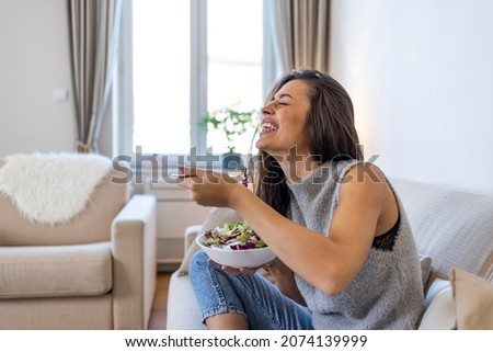 Eating healthy. Young woman eating salad. Young and happy woman eating healthy salad sitting on the table with green fresh ingredients indoors. Portrait of an attractive young woman eating a salad