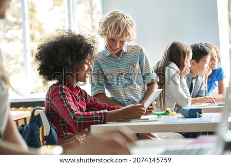 Happy smiling Caucasian boy and African American girl schoolchildren studying together using tablet device in classroom. Groups of schoolchildren working on task. Technologies for education concept. Royalty-Free Stock Photo #2074145759