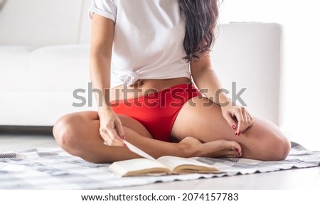 Detail of a woman wearing red period underwear sitting comfortably on the floor, reading a book. Royalty-Free Stock Photo #2074157783