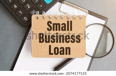 SMALL BUSINESS LOAN . blank notebook with markers pen beside. The notebook is on paper with text . Colored pencils and eyeglasses. Concept photo.