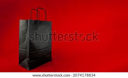 On a red background, isolated, is a black paper shopping bag. There is a lot of copy space.