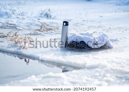 Thermos, slippers and a towel near the ice hole. Winter swimming. Hot drink in winter. Get warm with coffee. Ice and snow. Royalty-Free Stock Photo #2074192457