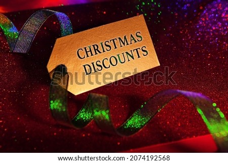 Gold color label with text - Christmas discounts, with bright green ribbon, bright festive luxury shiny red background. Christmas and New Year concept. 