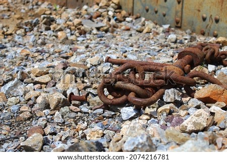 Rusty chain for towing or bundling large items.  laid on a pile of stones