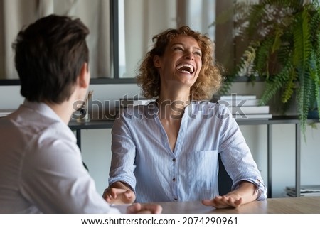 Cheerful young businesswoman laughing, enjoying pleasant conversation with colleague in modern workplace Happy sincere emotional employees having fun, entertaining during break pause time together. Royalty-Free Stock Photo #2074290961