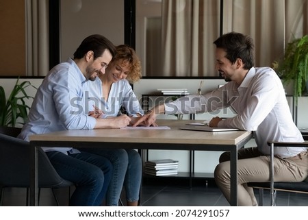 Smiling young professional lawyer financial advisor realtor showing place for signature on paper contract to happy millennial couple clients, satisfied with high quality service making deal agreement.