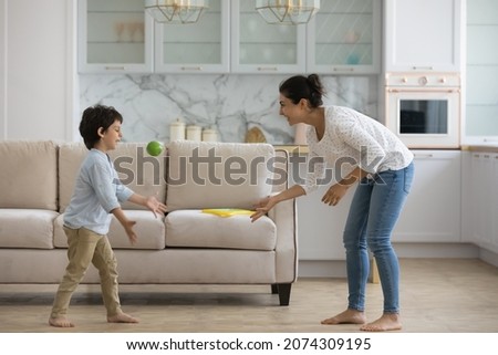 Excited Indian mom playing active games with little son at home, throwing ball to kid in living room, enjoying leisure with preschool boy. Babysitter watching child, practicing activity on playtime Royalty-Free Stock Photo #2074309195
