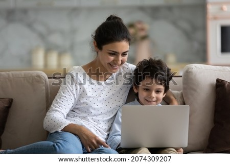 Happy Indian little son and loving mom enjoying leisure at laptop on couch, watching movie, using app, chatting online. Mother and child boy shopping on internet at home, talking on video call Royalty-Free Stock Photo #2074309207