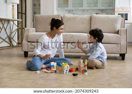 Loving young Indian mother and little son playing together on heating floor, building towers from toy construction bricks, talking, enjoying leisure, playtime, creative game. Motherhood concept Royalty-Free Stock Photo #2074309243