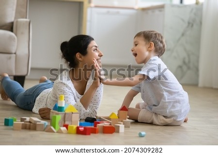 Happy nanny giving high five praise to excited preschool kid boy for completing toy tower on warm floor. Indian babysitter and kid playing at home, constructing building from small wooden blocks Royalty-Free Stock Photo #2074309282