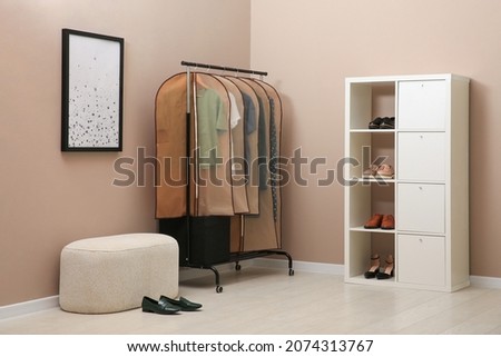 Garment bags with clothes hanging on rack in room Royalty-Free Stock Photo #2074313767