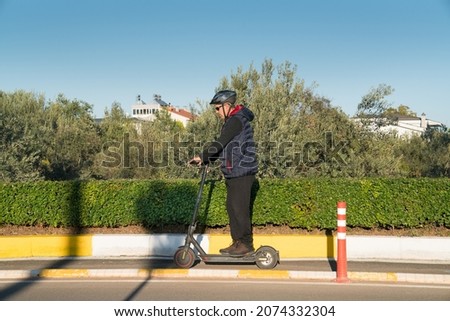 Mature man rides electric scooter on bike path in green field in autumn