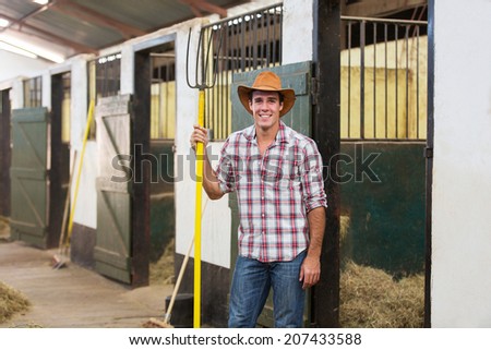 happy horse farmer holding pitch fork in stable