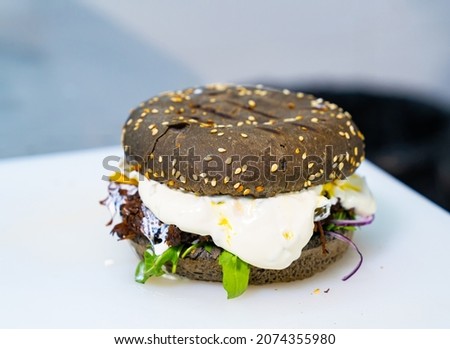 Appetizing black bun burger with fried egg. Brown bread for hamburger with sesame seeds on white background. Delicious fast food close-up.