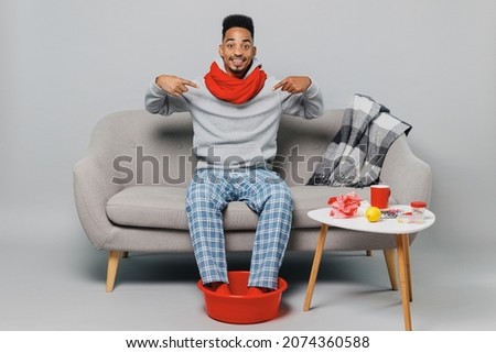 Young impressed happy african man in grey sweater scarf sit on sofa point index finger on himself isolated on plain gray background studio portrait Healthy lifestyle ill sick disease treatment concept