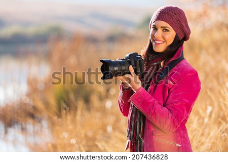 beautiful young woman holding a dslr camera outdoors in autumn