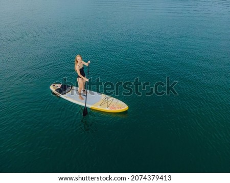 Young women Having Fun Stand Up Paddling in the sea. SUP. Red hair girl Training on Paddle Board near the rocks