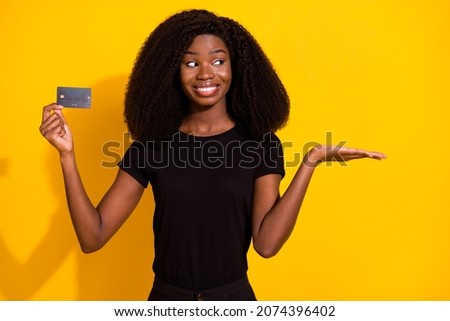 Photo portrait smiling woman showing credit plastic card keeping blank space on palm isolated vivid yellow color background