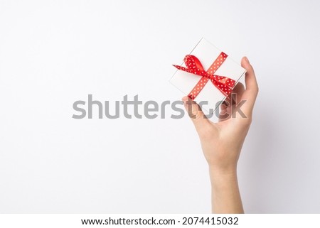 First person top view photo of female hand demonstrating small white giftbox with red dotted ribbon bow on isolated white background with empty space
