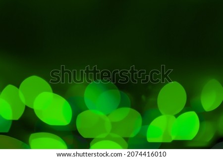 Defocused green lights over dark background. Natural bokeh and bright green lights. Magic background with bokeh. Space for text.