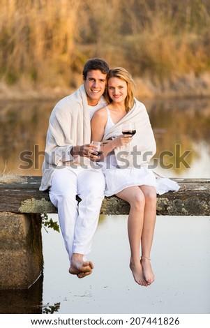 romantic couple sitting on pier and drinking wine at sunset