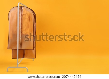 Garment bags with clothes on rack against yellow background. Space for text Royalty-Free Stock Photo #2074442494