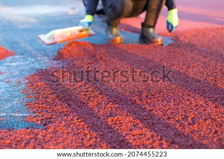 red rubber covering for the playground, the master smoothes the soft rubber crumb by hand. Soft covering for sports floors. Rubber mulch for safety and injury prevention. Royalty-Free Stock Photo #2074455223