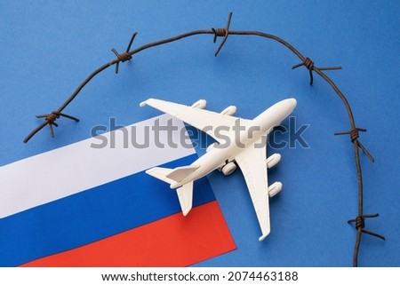 Russian flag, toy plane and barbed wire on blue background, concept of banning aircraft departing from Russia Royalty-Free Stock Photo #2074463188
