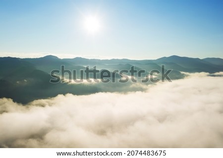 Aerial view of beautiful mountains covered with fluffy clouds on sunny day. Drone photography