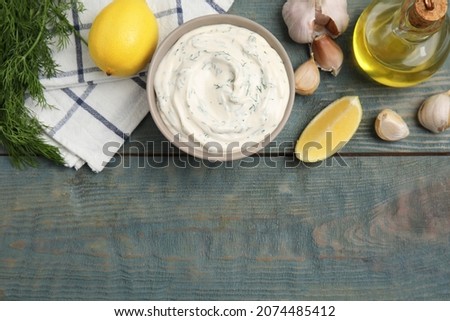 Tasty creamy dill sauce and ingredients on blue wooden table, flat lay. Space for text