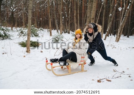 Couple in love, husband pushing a sleigh with his wife through the winter forest