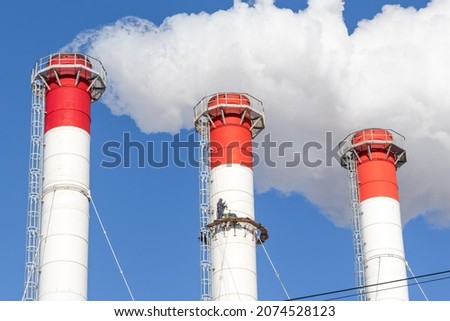 red-white chimneys of the boiler room, equipped with a traffic light. industrial climbers carry out routine repairs. white smoke on a blue sky background Royalty-Free Stock Photo #2074528123