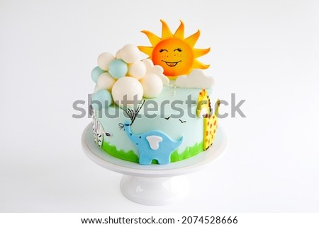
Baby birthday cake decorated with sun, clouds, elephant, giraffe, zebra animal figurines and balloons.
