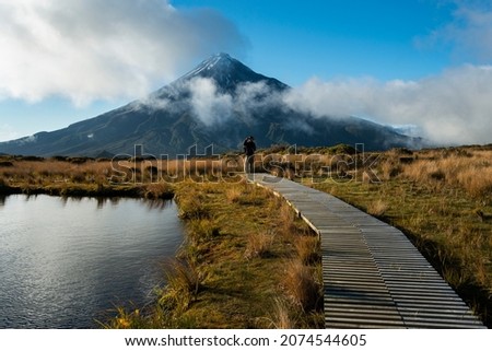 Hiker standing on the wooden boardwalk platform around the Pouakai tarn. Mt Taranaki in the background.  