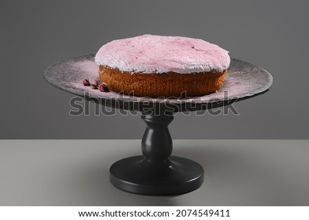 Bundt cake or sweet pie with decorated icing pink sugar from roses on a wooden stand with plate. Shallow depth of field